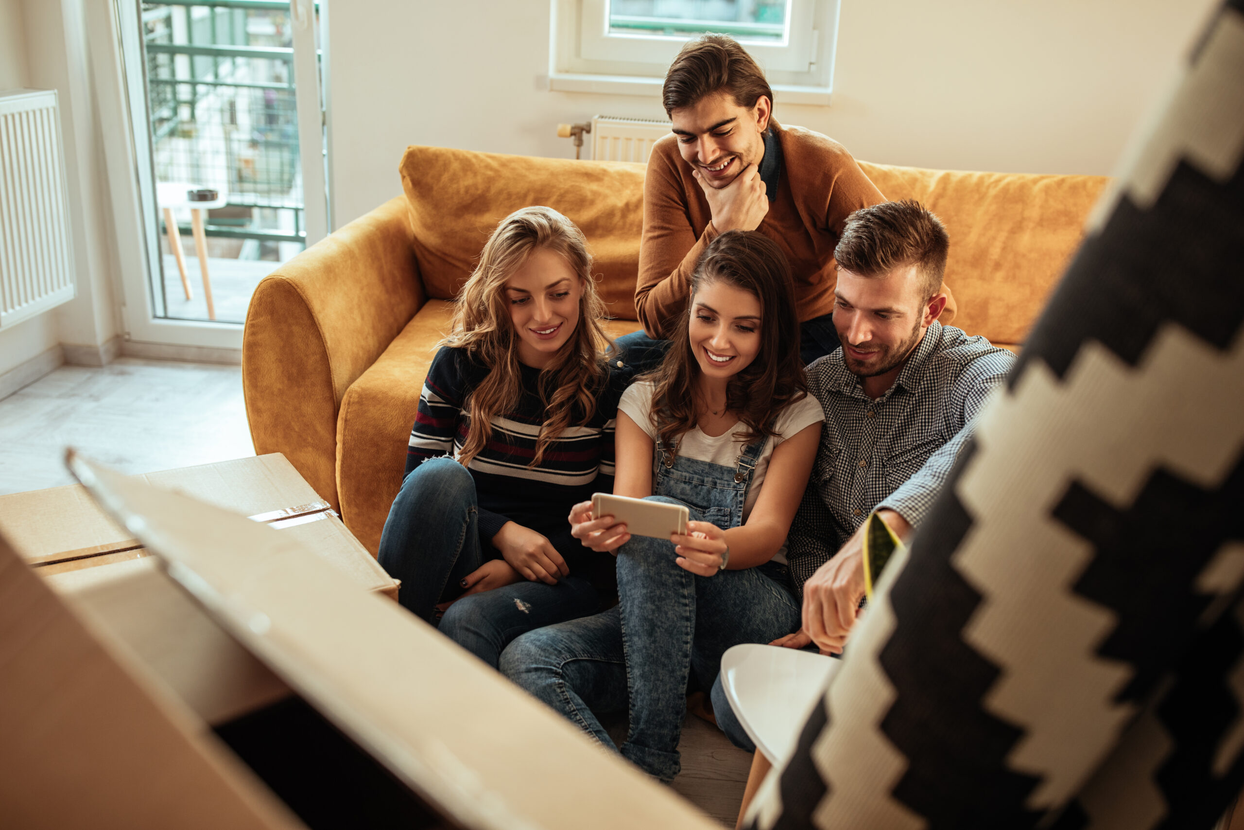 Group of friends using phone during moving in new apartment
