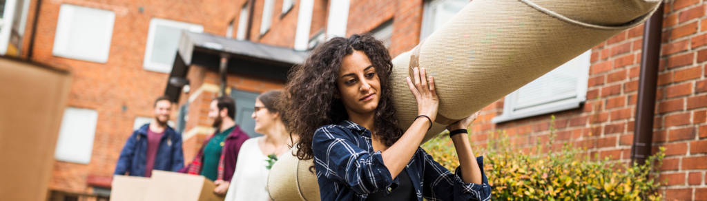 Ung kvinna som bär en ihoprullad matta i en flyttsammanhang