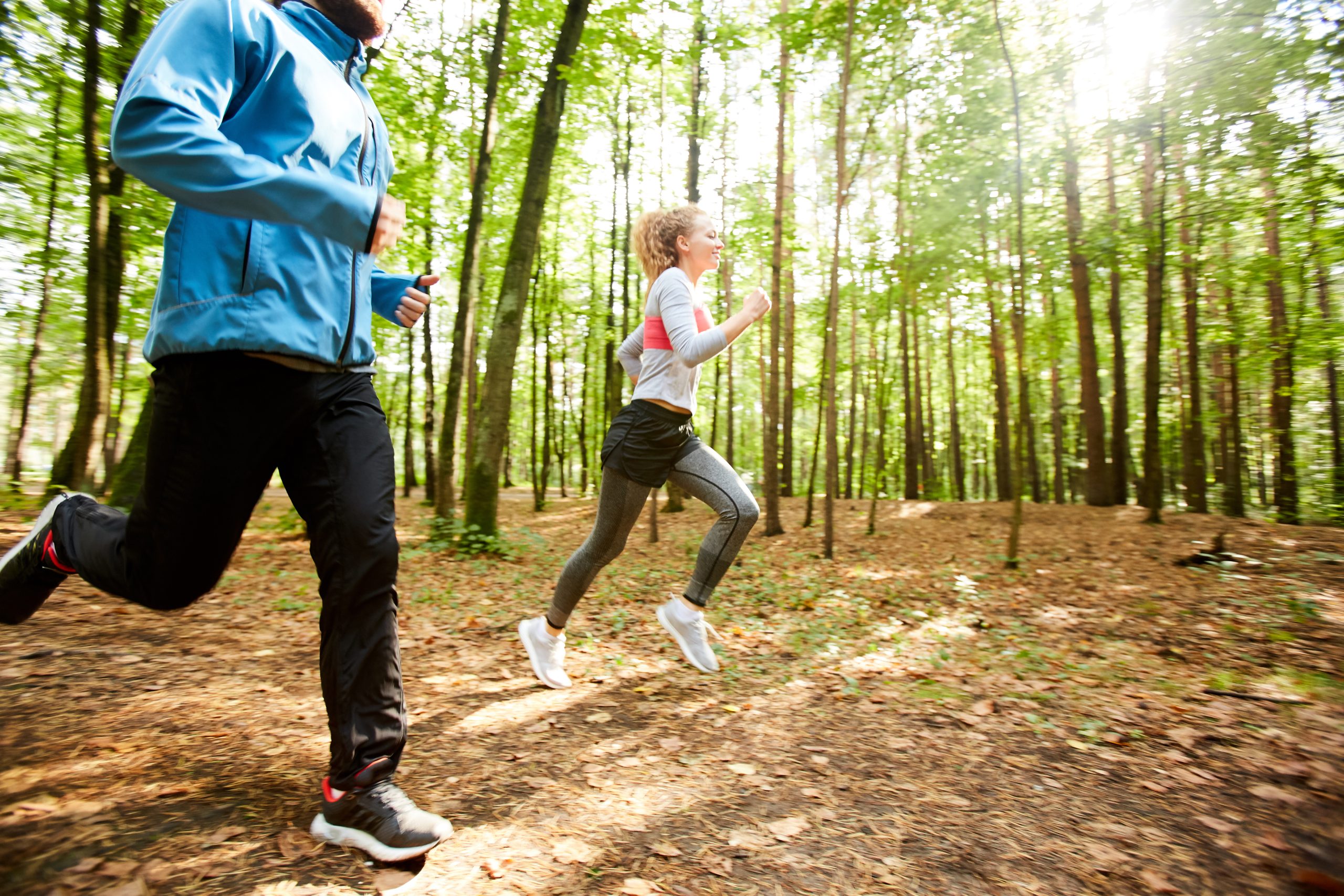 Active guy and girl in sportswear running down forest road while training in the morning