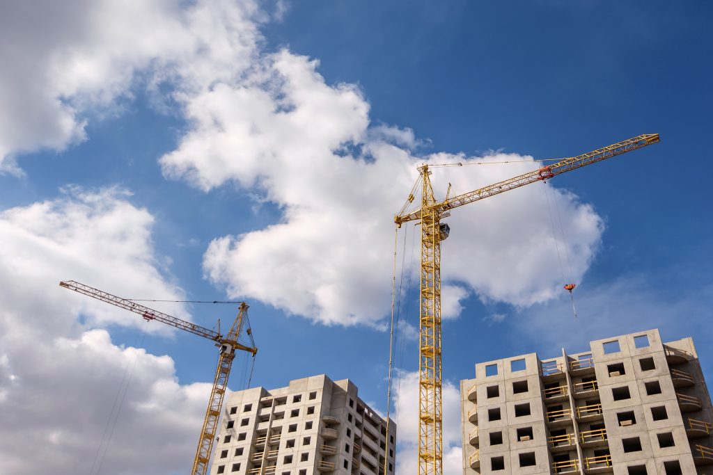 Tower cranes and unfinished multi-storey high near buildings under construction site in the sunny day with beautiful clouds