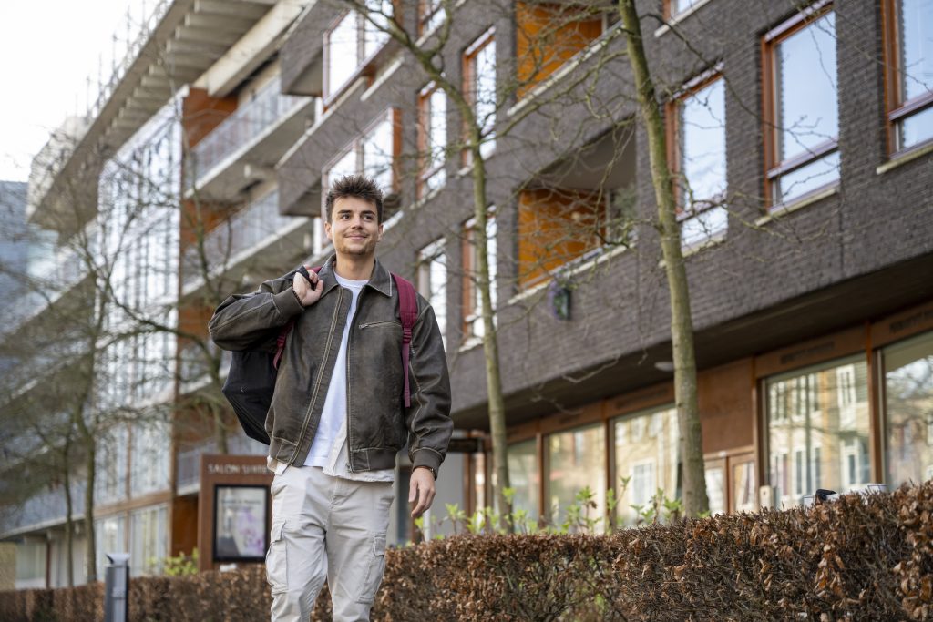Smiling young man walking in front of a residential building