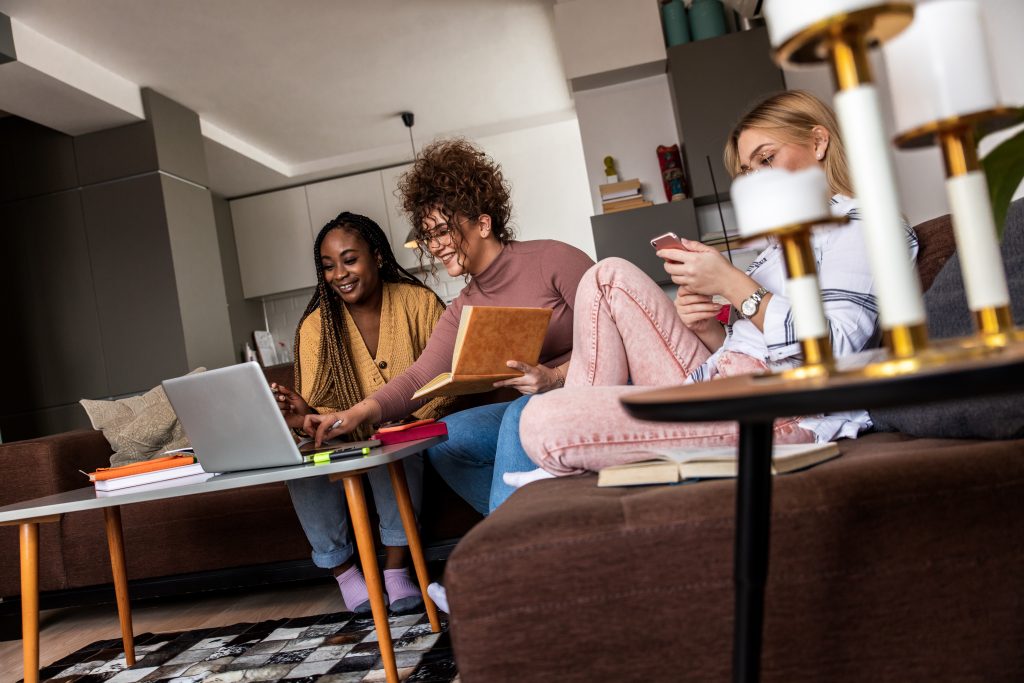 Diverse group female students learning at home using laptop and books for research.