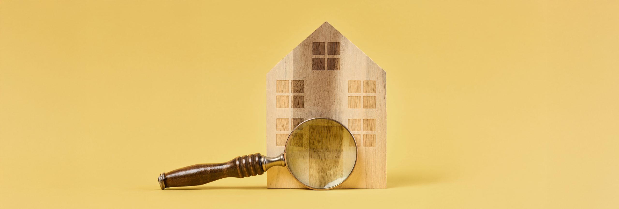 Wooden house and a magnifying glass, representing the concept of real estate purchase, rental growth, and mortgage interest